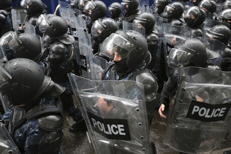 Mehrere behelmte Polizeikräfte mit Schilden stehen in Formation. 