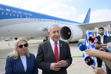 Der israelische Ministerpräsident Benjamin Netanjahu steht mit seiner Frau vor einem Flugzeug und gibt der Presse ein Interview.