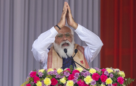Narendra Modi steht an einem Rednerpult und hat die Arme über den Kopf erhoben